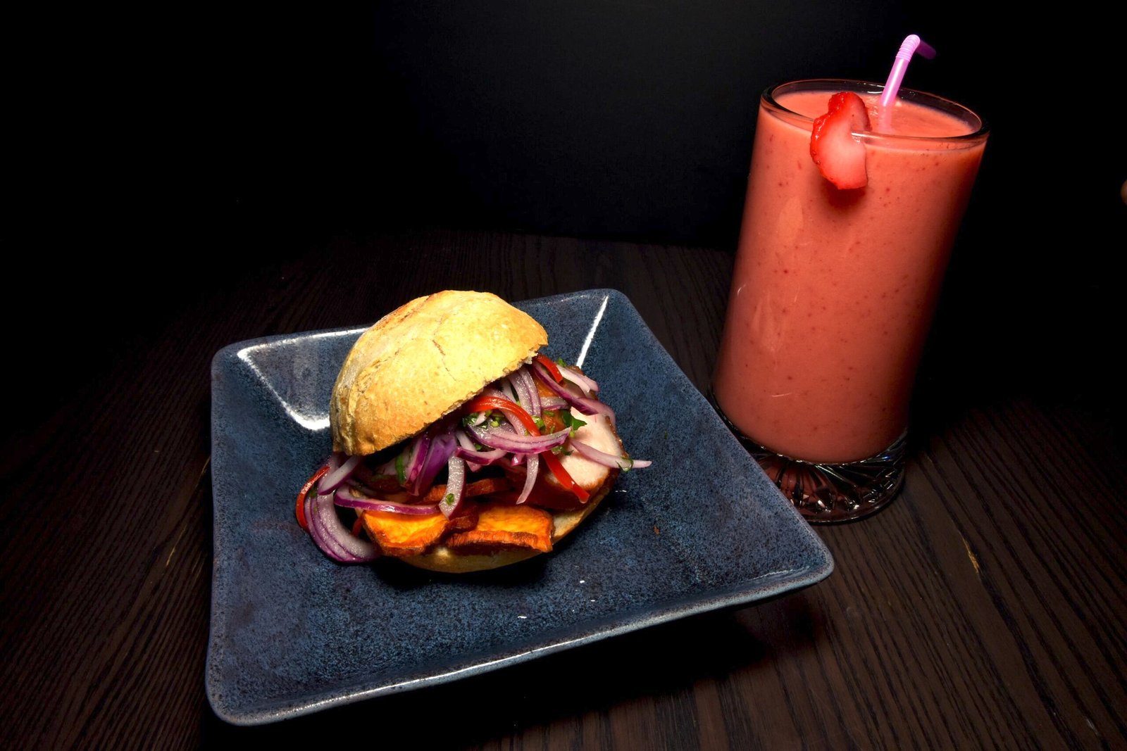 Bocata en pan de hamburguesa estilo tradicional relleno de ensalada y plátano frito. Al lado un batido de fresa.