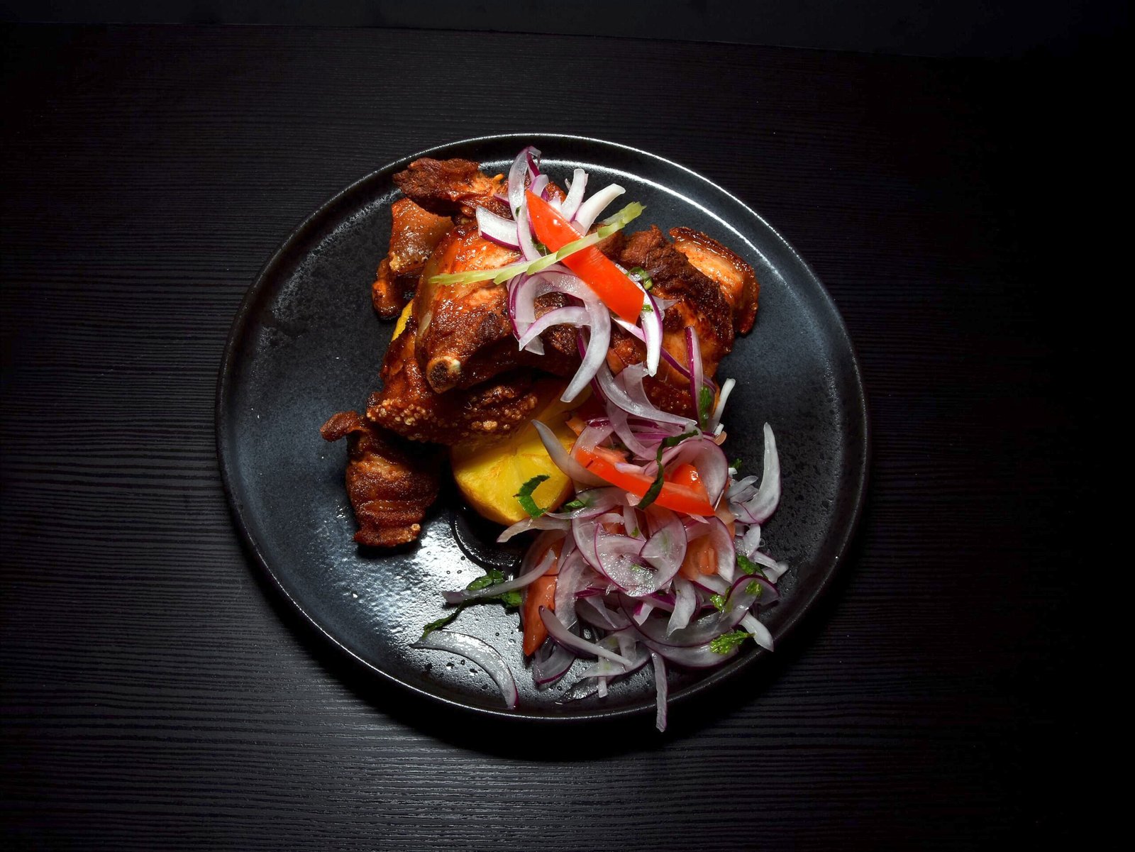 Chicharrón de cerdo acompañado de patata y ensalada de cebolla morada y tomate.